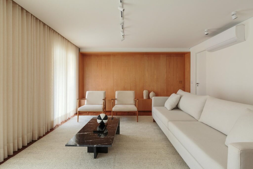 Sala de estar de apartamento de 250 m² com painel em madeira, sofá claro e duas poltronas